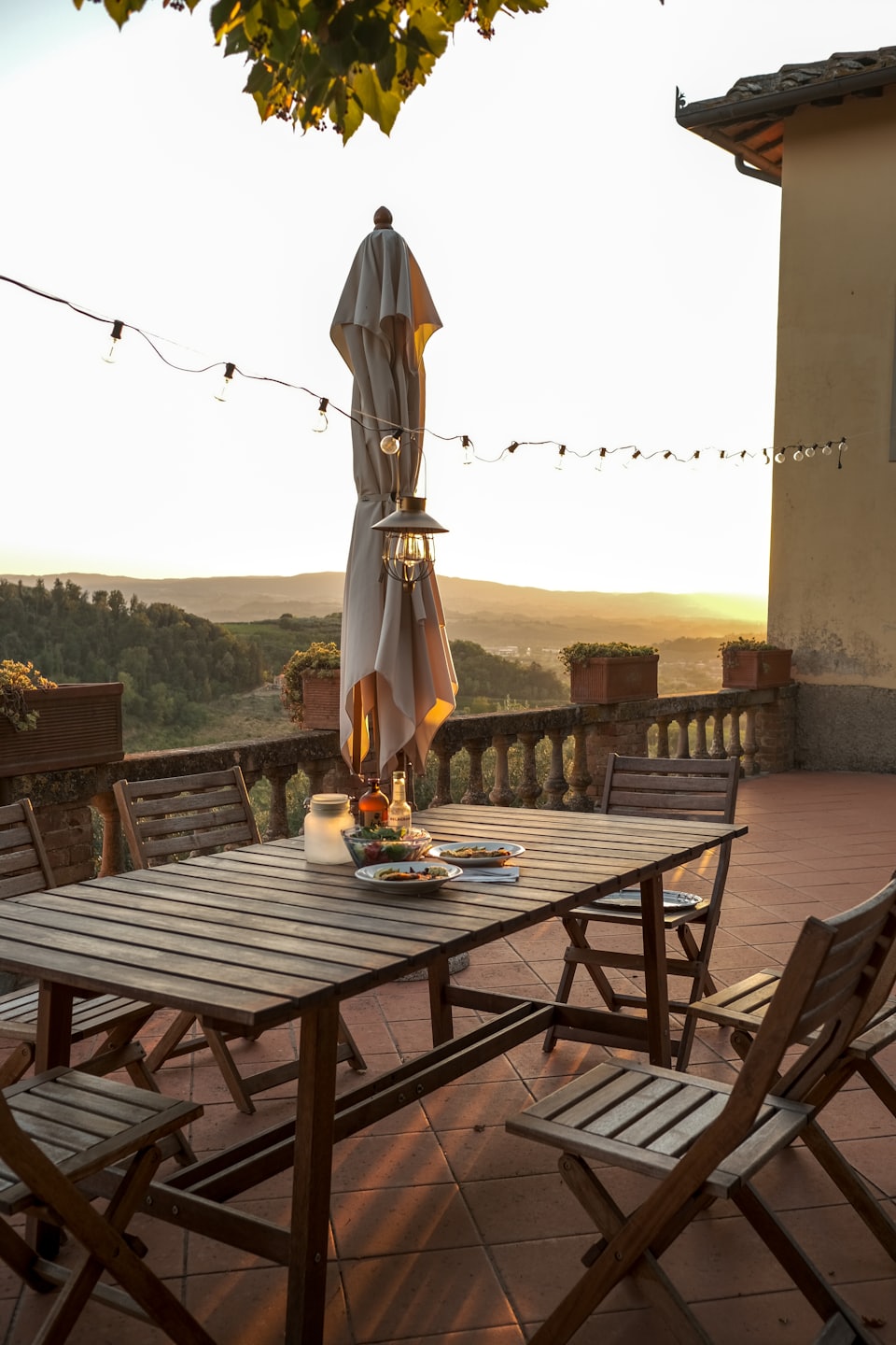 Tavolo da pranzo all'aperto su una terrazza con cibo e bevande, con vista sulle colline al tramonto.