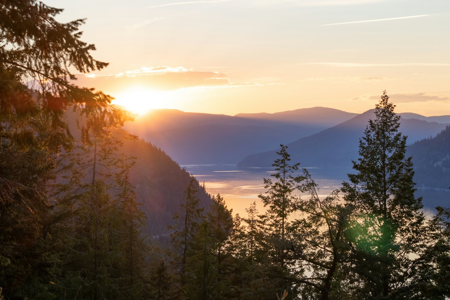 Il sole tramonta dietro le montagne, riflettendosi su un lago calmo.