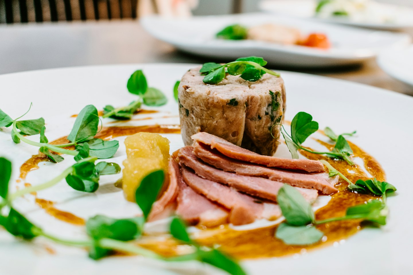 Piatto gourmet di carne con relish giallo e microgreens su piatto bianco.